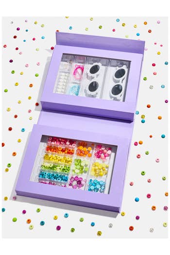 A bead kit with assorted colorful beads, strings, and tools arranged successful  an unfastened  purple container  connected  a scattered bead background