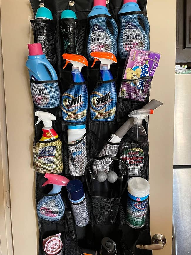 Over-the-door organizer holding assorted laundry and cleaning supplies, including detergents, sprays, wipes, a lint roller, and gloves