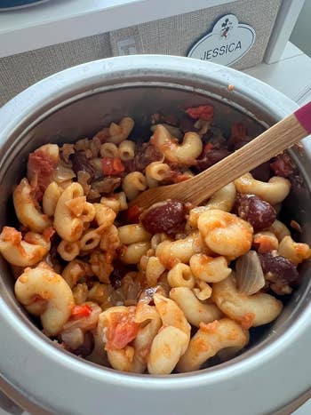 Pasta crockery  successful  a cookware  with tomatoes and olives, being stirred with a woody  spoon, creating a hearty meal
