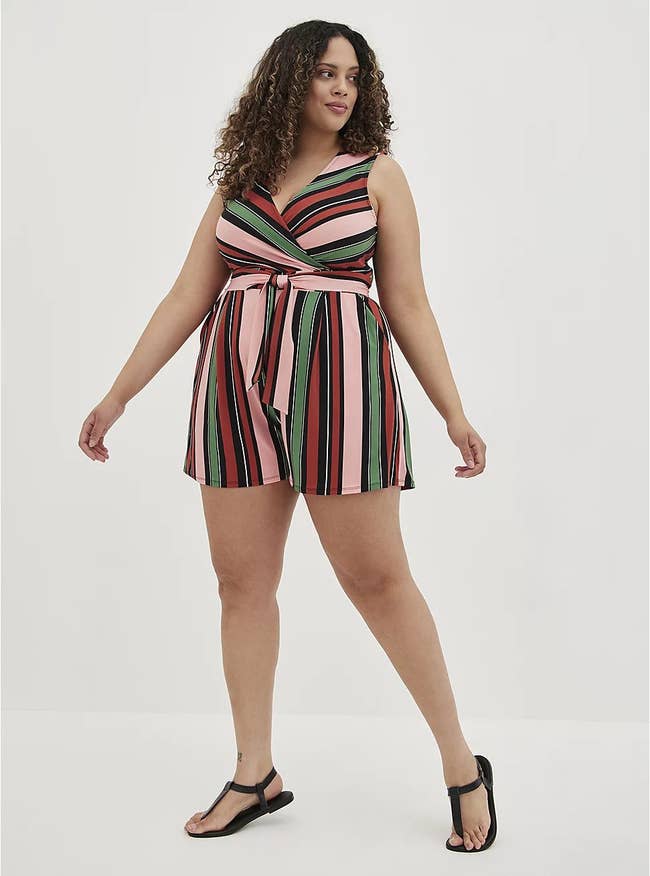 model in sleeveless pink, red, and green striped romper and black sandals