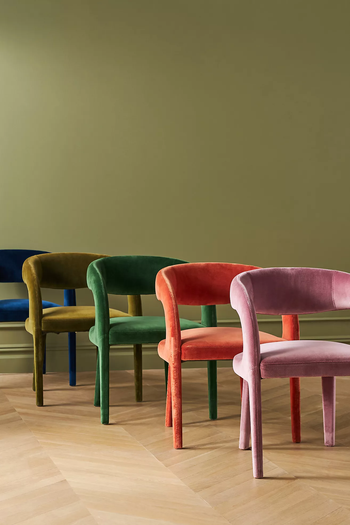 Four velvet chairs in varying designs and shades placed against a green wall