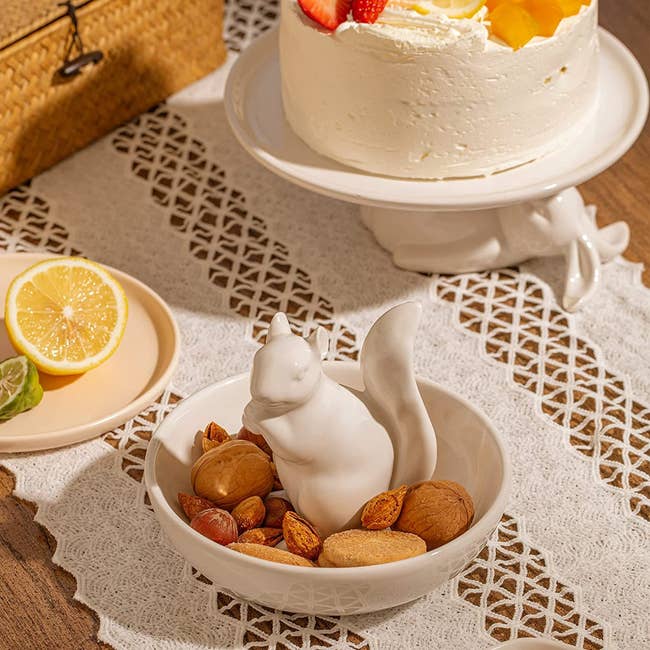 white dish with ceramic squirrel in center. dish is filled with nuts. 