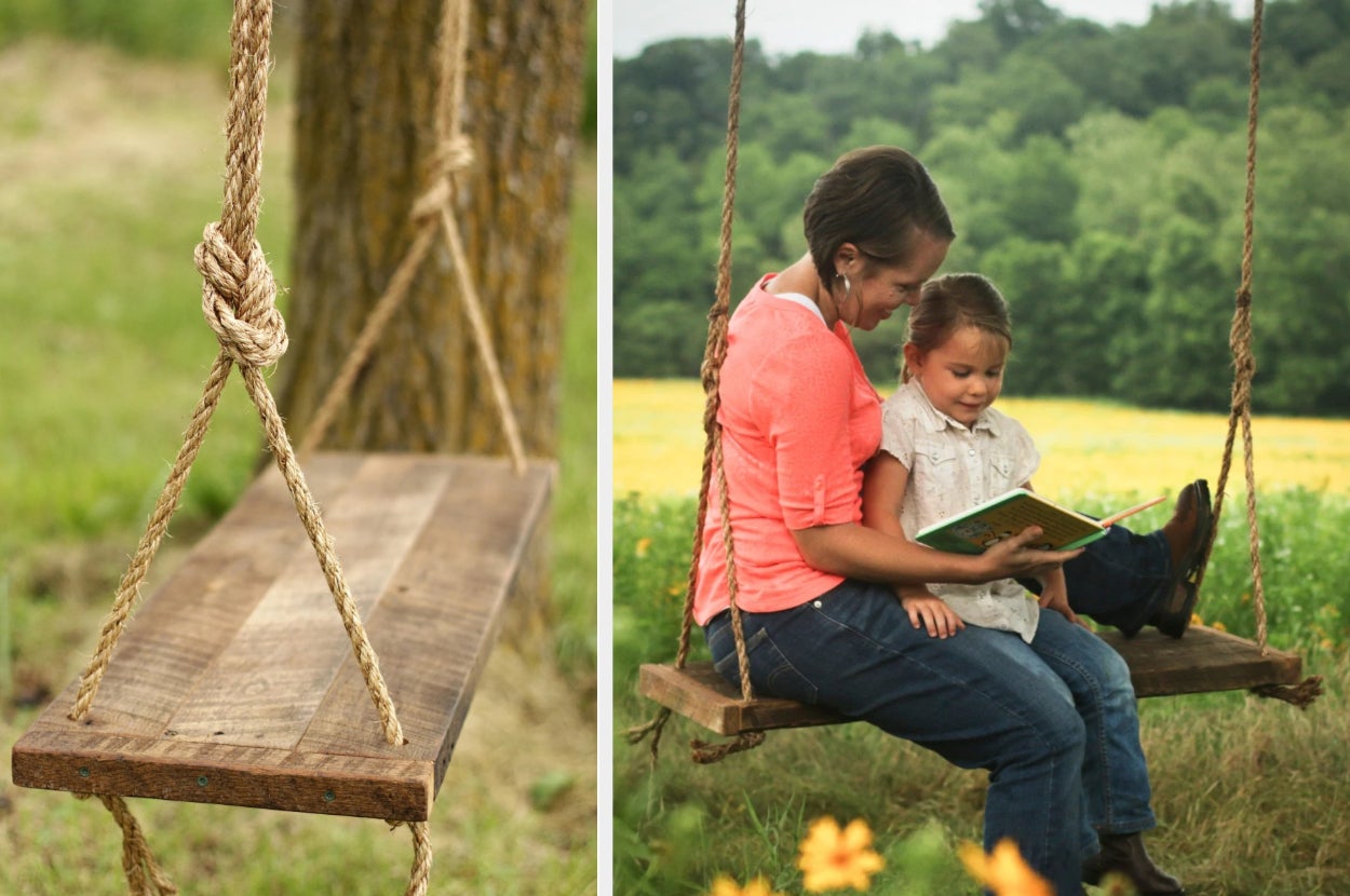 Wooden outdoor swing with rope handles next to a tree, models sitting on product in a field reading a book