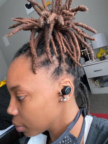 Person with twisted updo hairstyle wearing wireless earbuds and a nose ring, side profile view