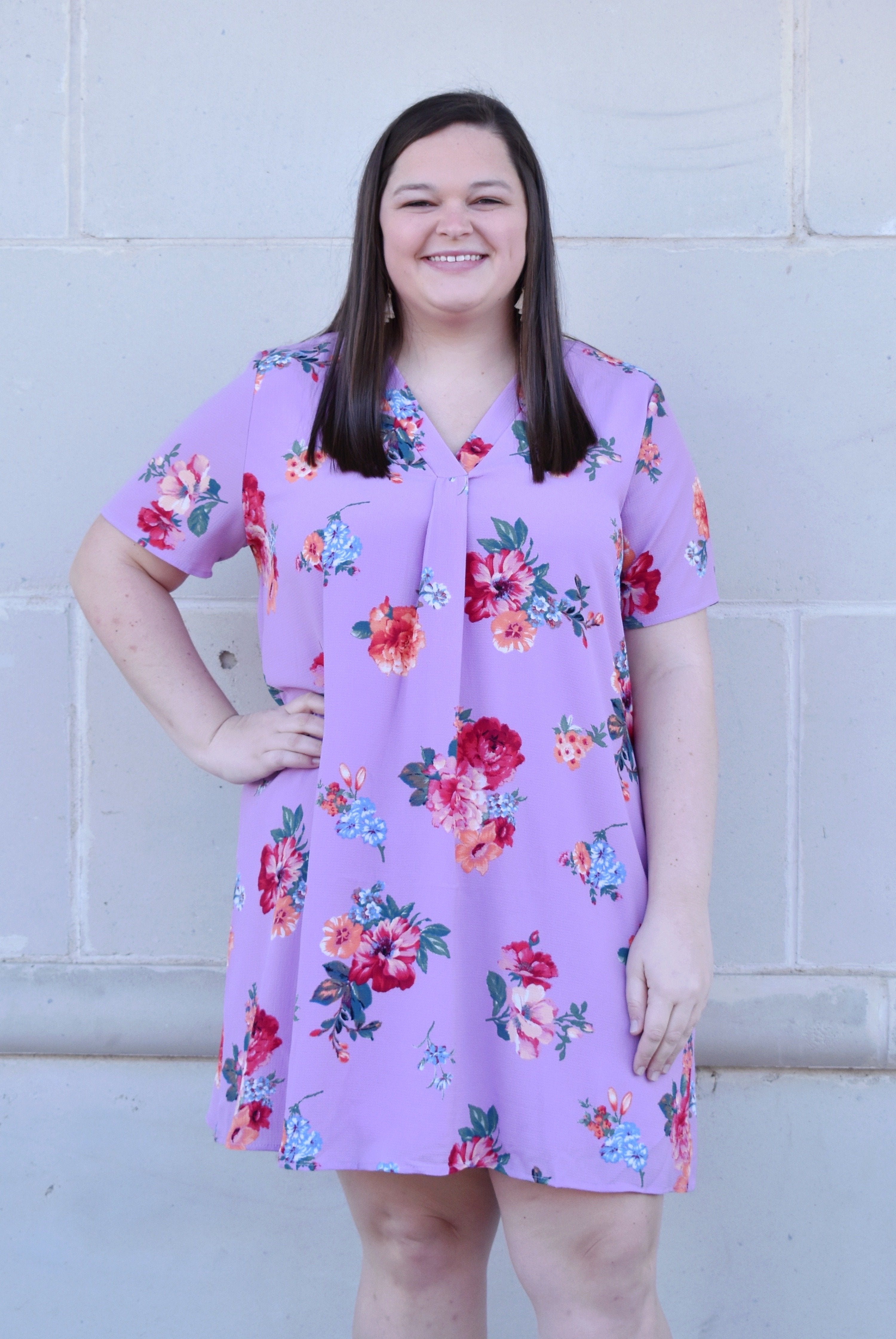 reviewer in v-neck short sleeve lavender dress with blue, pink, red, and orange flowers and a pleat at the neckline