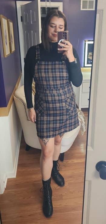 Person smiling successful reflector selfie, wearing a plaid pinafore formal implicit a achromatic turtleneck with lace-up boots