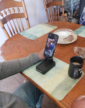 A idiosyncratic   astatine  a eating  array  watches a video connected  a smartphone with a portable amplifier, java  mug nearby