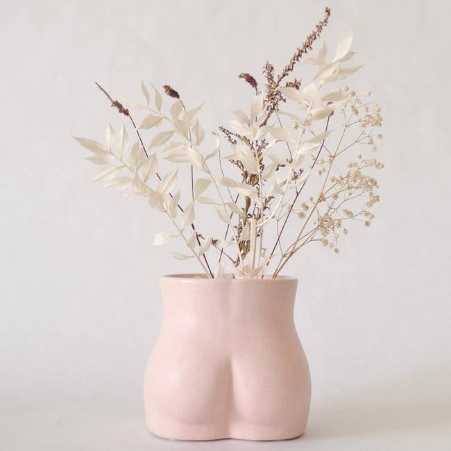 Pink ceramic vase shaped like a butt with flowers in it