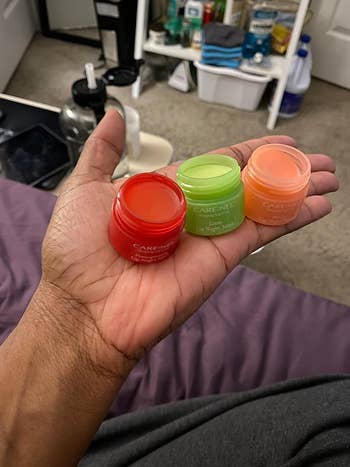 reviewer holding the three containers of the lip mask in red, green, and orange