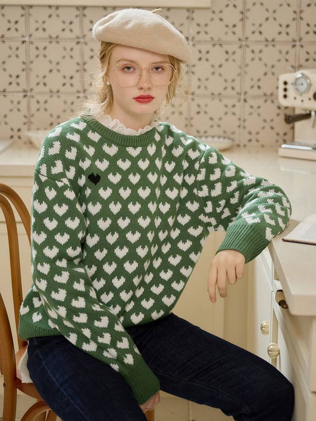 a model in a green sweater with knit white hearts on it