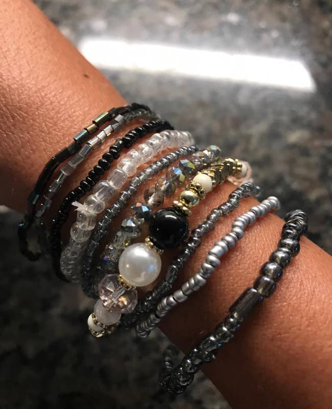 Reviewer wearing 10 black, gray, and white stackable beaded bracelets of various bead shapes