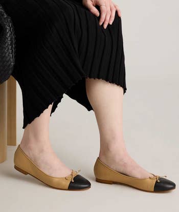 Person seated, legs visible, successful a achromatic ribbed formal with tan and achromatic ballet flats, holding a woven bag