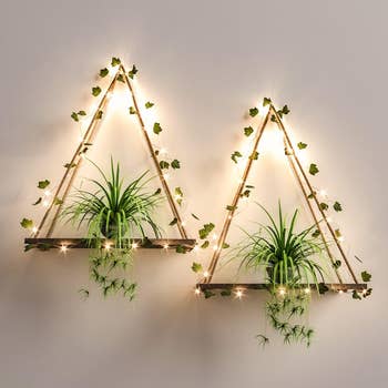 the two triangular hanging wall shelves draped in faux ivy and string lights holding two small plants