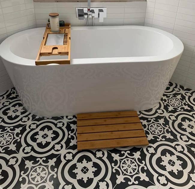 Freestanding bathtub with wooden mat in front of it 
