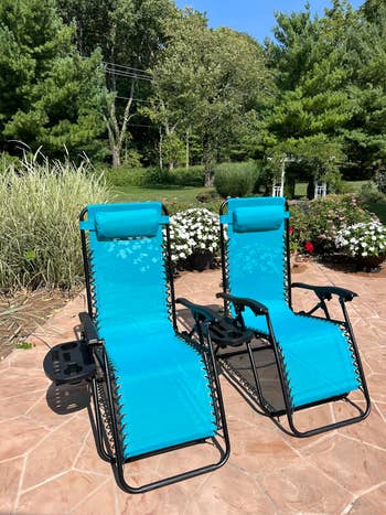 Two reclining outdoor lounge chairs connected a patio, acceptable against a plot with trees and flowers