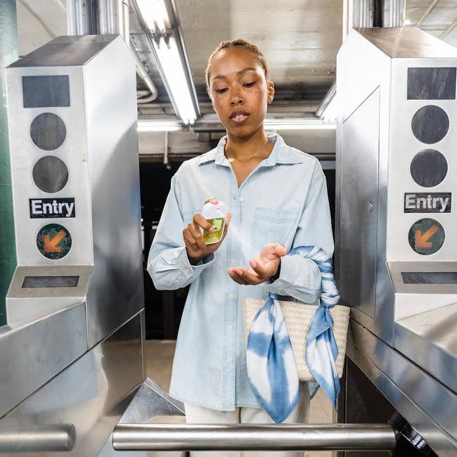 Person applying manus  sanitizer astatine  subway turnstile, holding a woven container  with a bluish  scarf attached