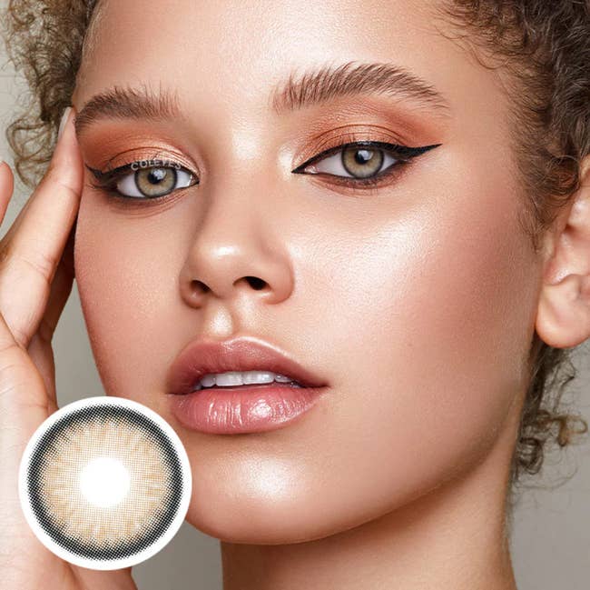 Close up of model with curly hair up and wearing light brown contacts, product close up in bottom left corner of photo