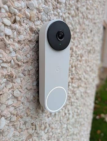 Smart video doorbell mounted connected a textured wall, featuring a circular camera and a fastener below
