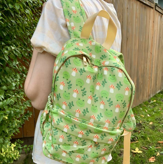 model wearing green backpack with mushroom and frog prints