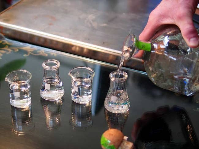 a model pouring tequila into a set of mini beaker shot glasses