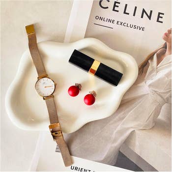 Watch, lipstick, and reddish  earrings connected  a tray; a mag  showing a overgarment  titled 
