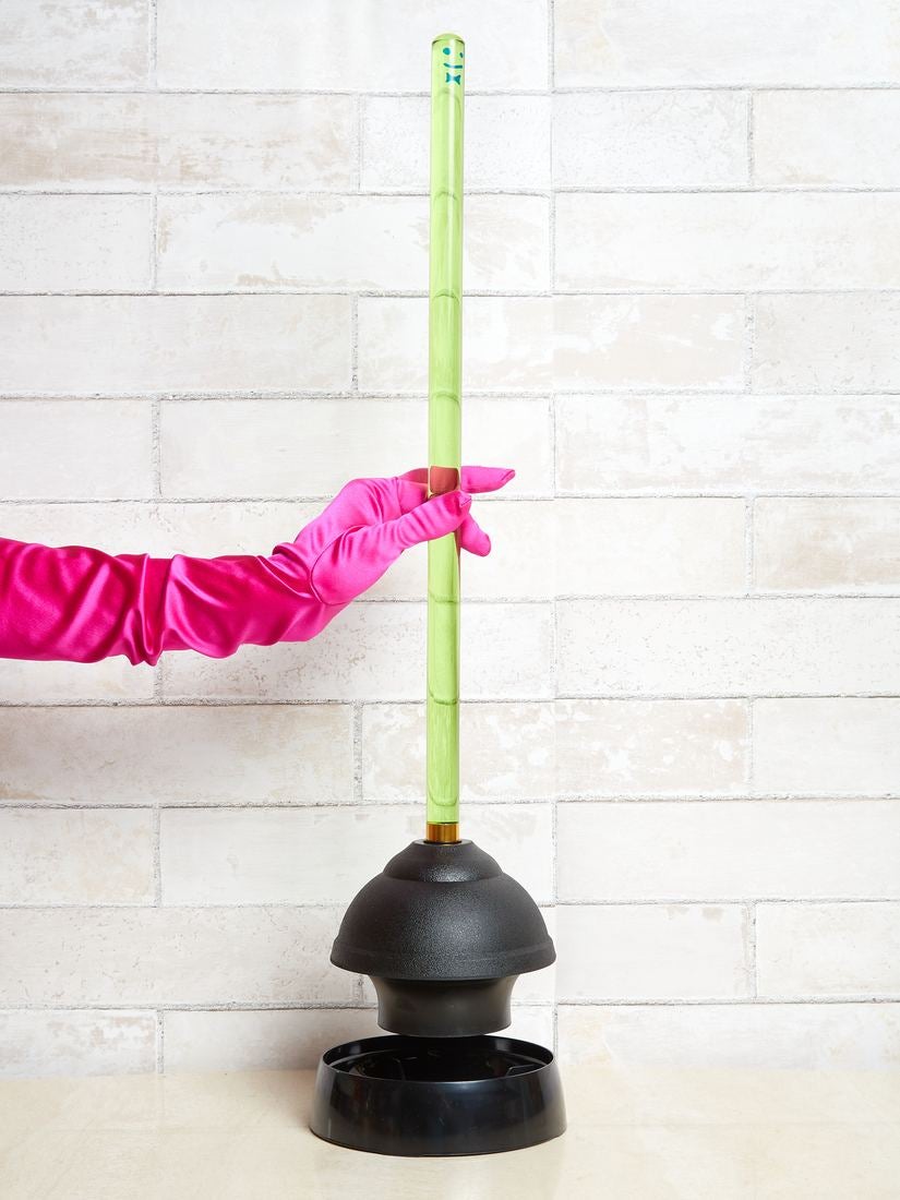 a hand wearing a pink satin glove picks up the green plunger
