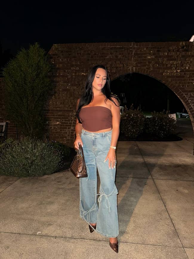 Person wearing a strapless apical  and flared jeans, holding a patterned handbag outdoors