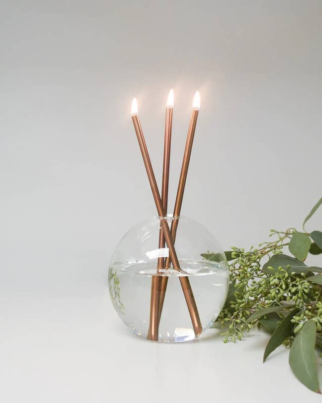 round orb filled with oil and three metal candle sticks 