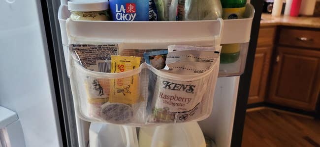 Refrigerator door with condiment packets, including Ken's Raspberry Vinaigrette, in a mesh organizer, next to a milk carton
