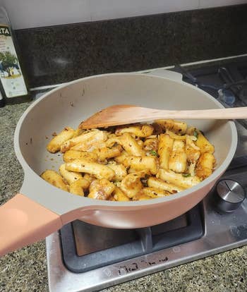 Cooked pasta with herbs in a pan on a stove, wooden spatula inside