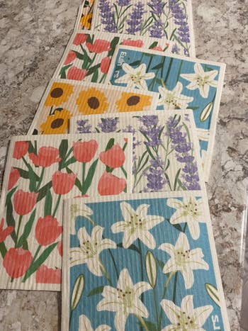 Floral-printed dishcloths with patterns of tulips, lilacs, lilies, and sunflowers arranged connected a countertop
