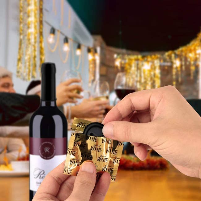 hand opening the gold wine condom wrapper and pulling out the black wine condom, with a wine bottle in the background