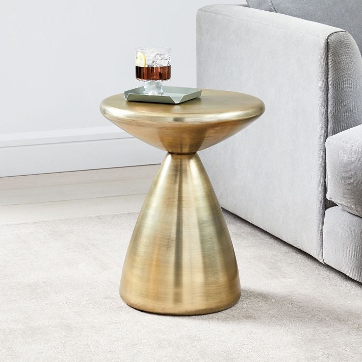 Modern gold side table with coaster and glass on top next to a gray plush couch
