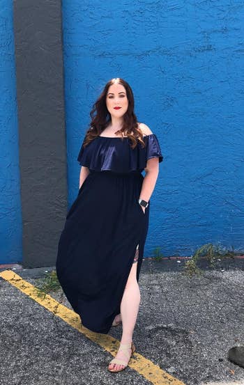 Reviewer wearing the off-the-shoulder ruffle maxi dress in navy blue with a slit up the side.
