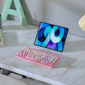 A pink retro-style keyboard with purple and yellow keys next to a tablet screen 