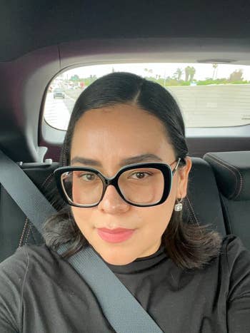 Person wearing stylish large glasses and a black top, seated in a car