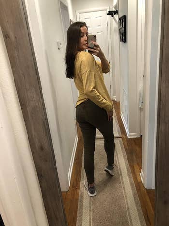 A reviewer taking a mirror selfie in a hallway, showcasing their outfit of a casual yellow top, olive green pants, and white sneakers
