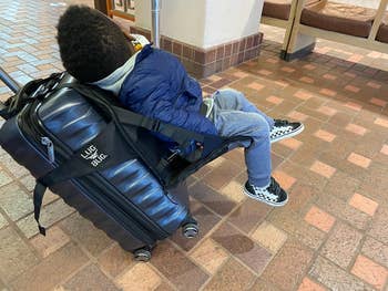A child sitting on a seat attached to luggage 