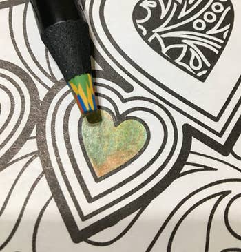 Close-up of a coloring book with heart being colored with a multicolored pencil