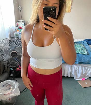 Person takes a mirror selfie wearing a white top and red leggings