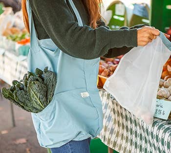 a model with the tote in blue on their shoulder holding a drawstring produce bag 