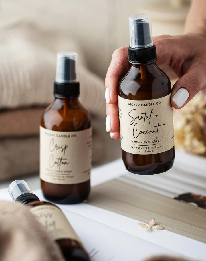 a model holding a bottle of room spray next to two other bottles of room spray in different scents