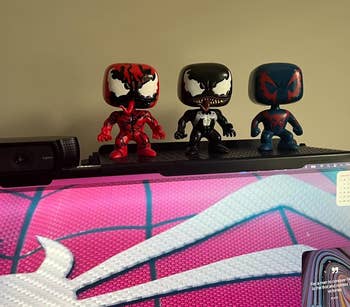 Three Funko Pop figures, resembling Spider-Man variants, displayed on top of a monitor