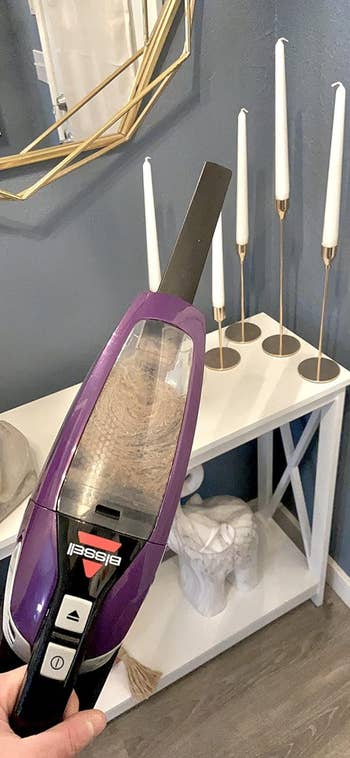 Handheld vacuum cleaner filled with dirt in a home setting with decorative items in the background