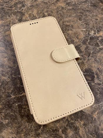 Reviewer image of white leather phone case with magnetic closure on top of a counter