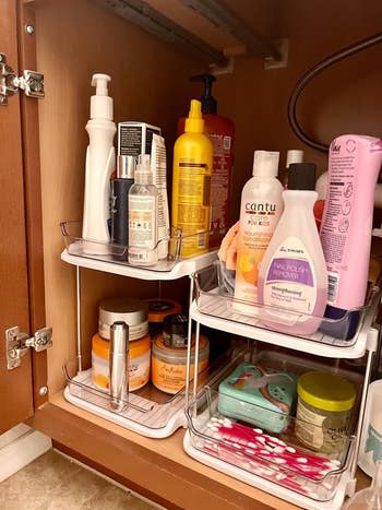 reviewer showing two white organizers under sink cabinet holding various toiletries