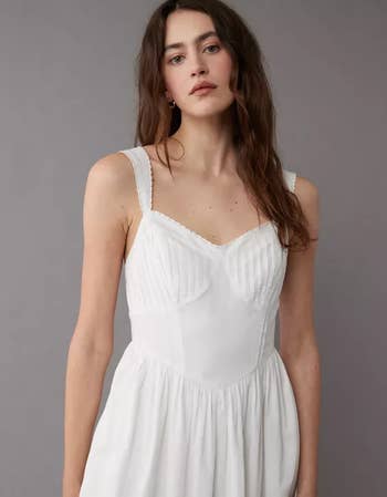 Model poses in a simple white sundress with delicate straps and a V-neckline