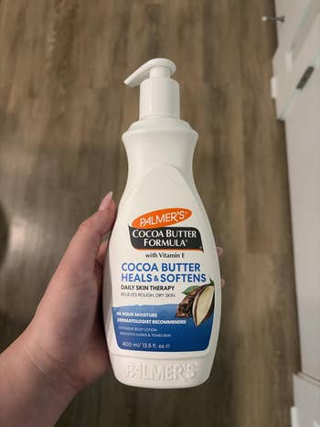 Person holding a vessel  of Palmer's Cocoa Butter Formula, known for moisturizing and softening adust  skin