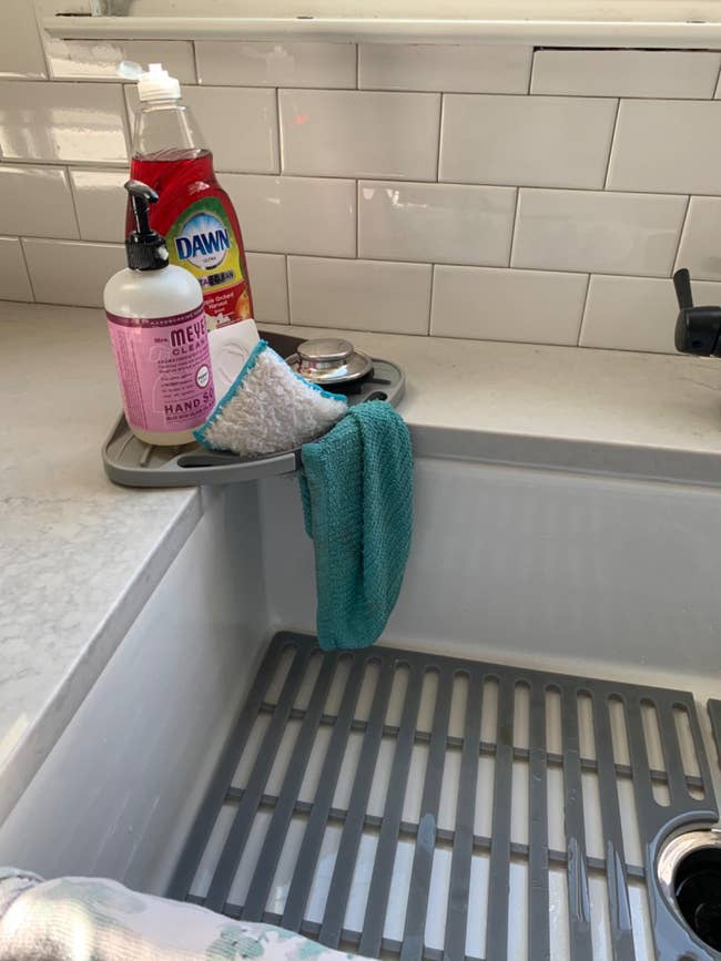 A kitchen sink with Mrs. Meyer&rsquo;s hand soap, Dawn dish soap, a sponge, and a turquoise dishcloth