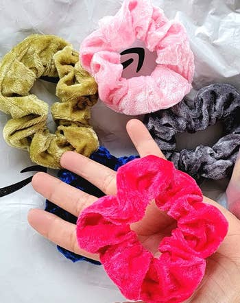 reviewer holding a hot pink velvet scrunchie next to four other scrunchies in other colors